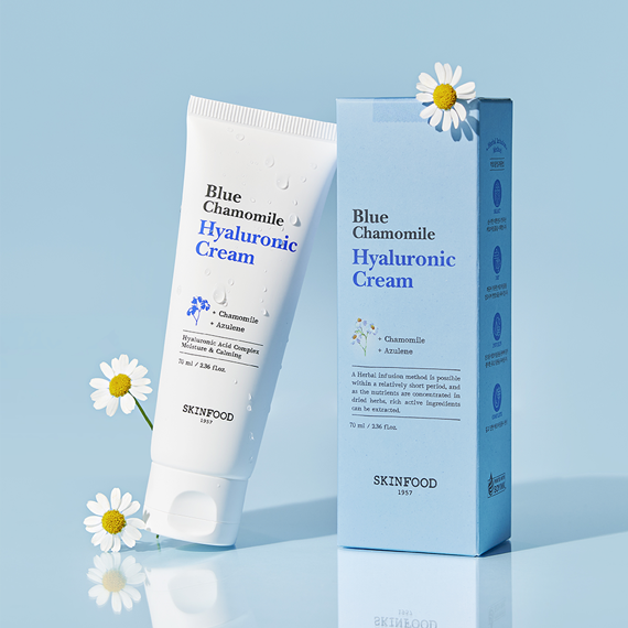 SKINFOOD Blue Chamomile Hyaluronic Cream 70ml de SKINFOOD, tube et boîte sur fond bleu, fleurs camomille en déco.