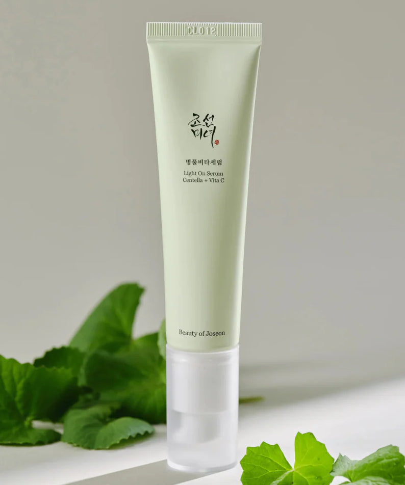 Décris l'image en français : BEAUTY OF JOSEON Light On Serum Centella+ Vita C 30ml sur fond beige avec feuilles vertes.