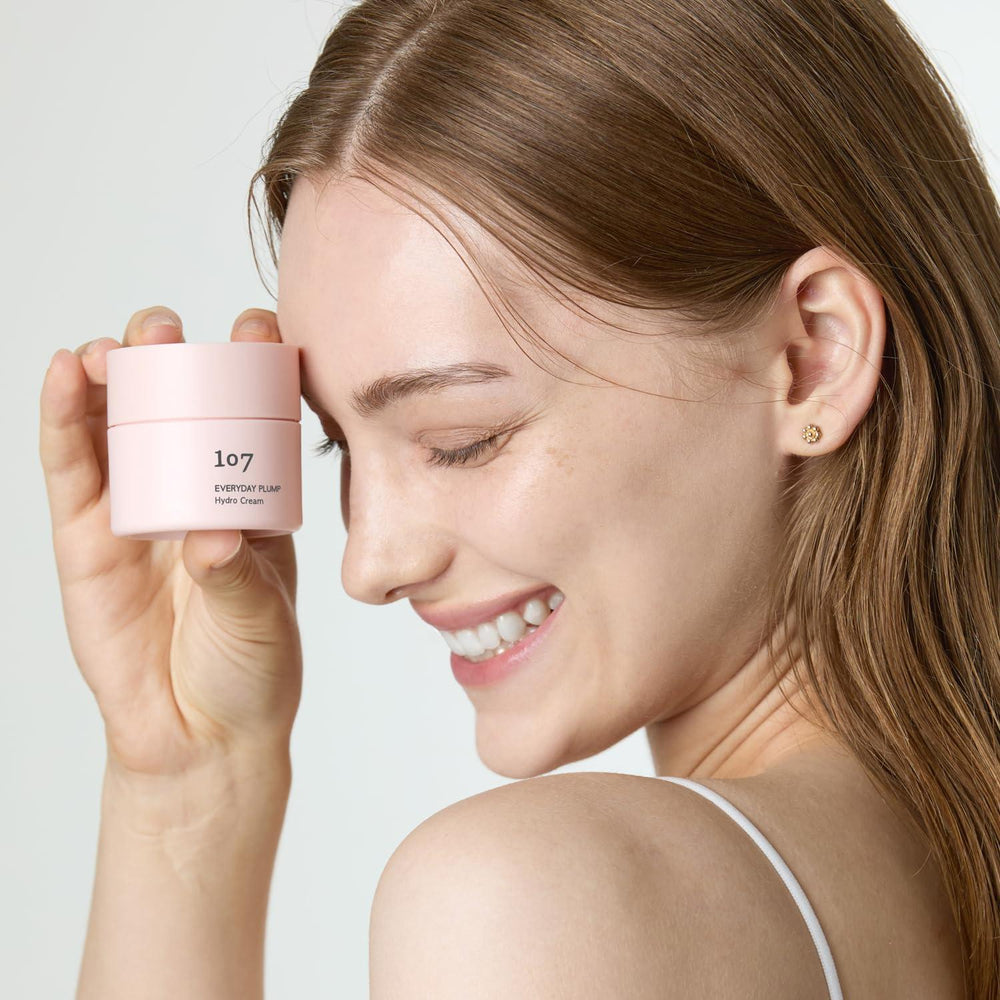Décris l'image en français : 107 Everyday plump Hydro Cream 50ml de la marque 107, pot rose, visage souriant fond clair.