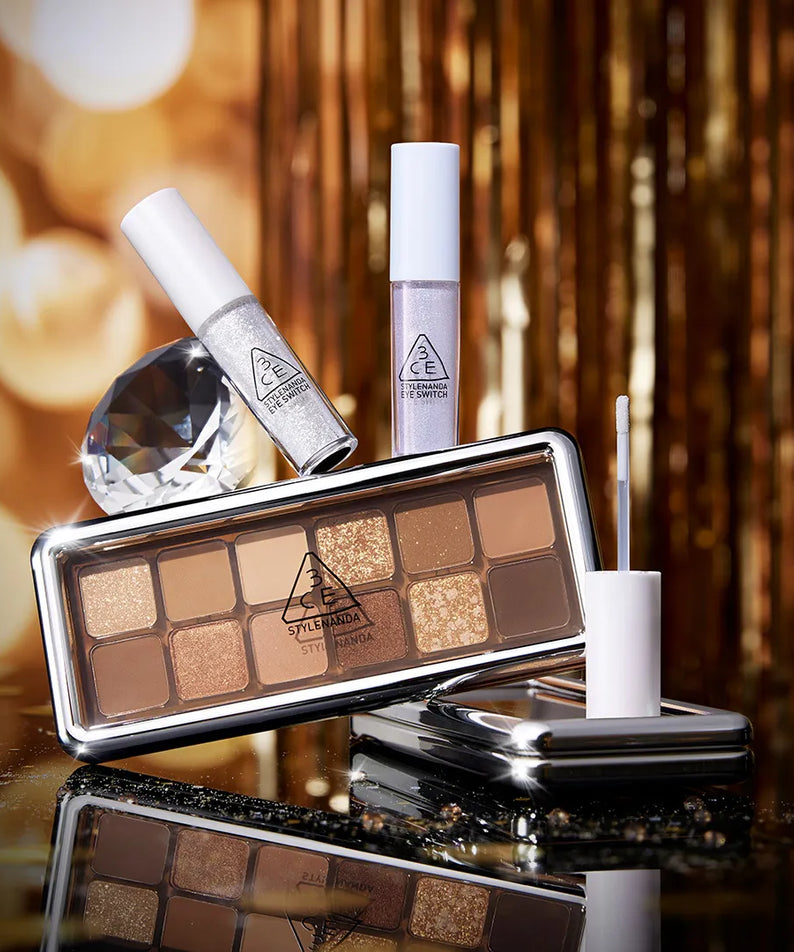 3CE  Eye Switch de 3CE, palette et stick sur fond doré, ambiance maquillage glam