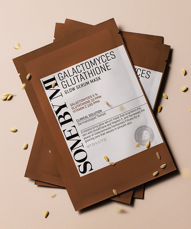 Décris l'image en français : SOME BY MI Galactomyces Glutathione Glow Serum Mask, masques SOMEBYMI sur fond clair avec détails dorés.