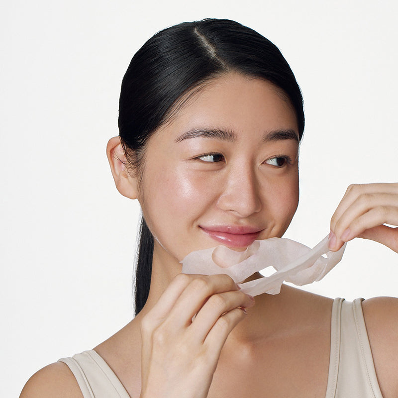 SOME BY MI Galactomyces Glutathione Glow Serum Mask : femme pose une feuille de masque visage sur fond blanc, marque SOME BY MI