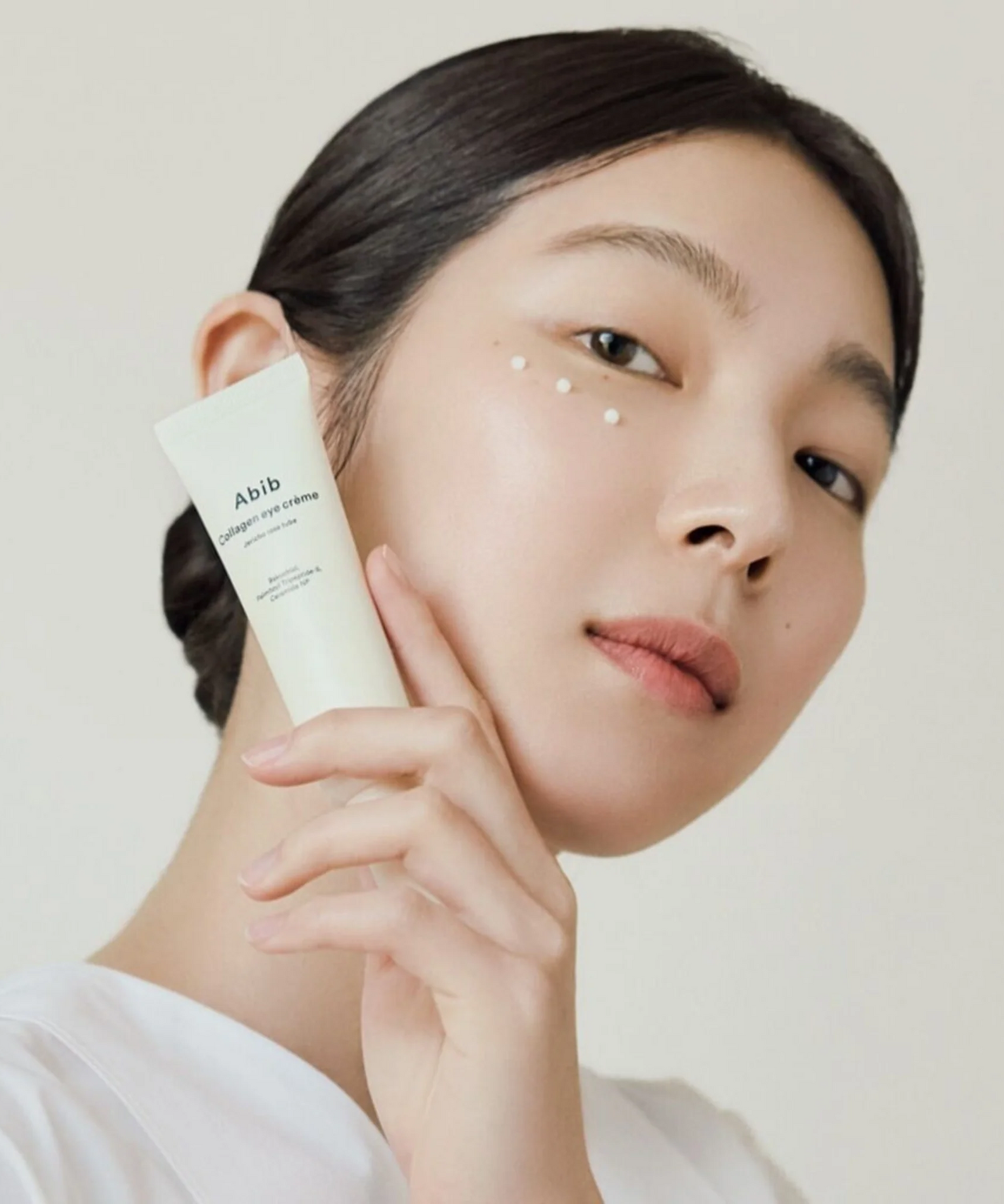 ABIB Collagen Eye Cream Jericho Rose Tube 30ml : femme applique une crème contour des yeux sur peau claire, fond clair.