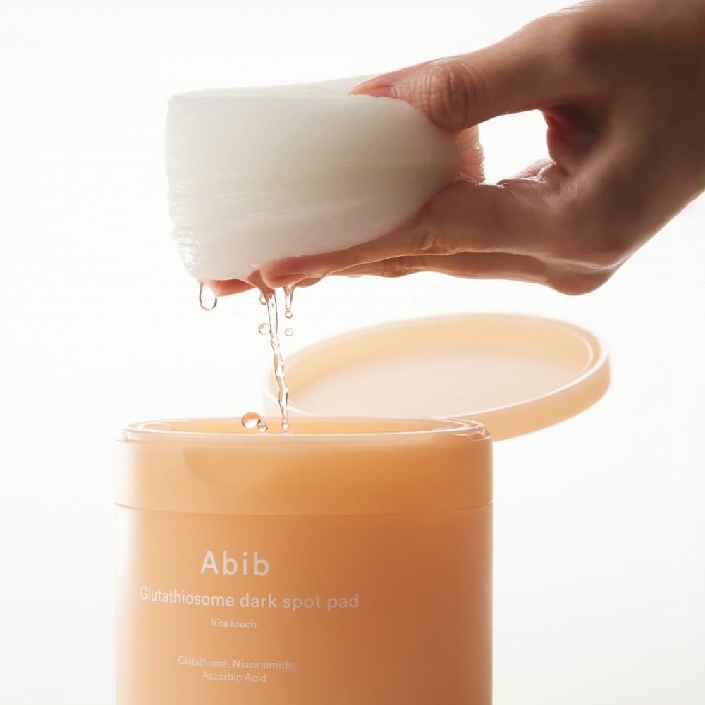 Photo en gros d’une main tenant ABIB Glutathiosome Dark Spot Pad Vita Touch 60 EA, marque Abib, face crème sur fond clair