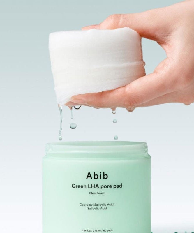 Main tenant ABIB  Green LHA Pore Pad Clear Touch 60 Sheets, coussin vert pour pores, sur fond clair, marques Abib visibles.