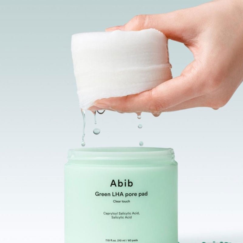 Main tenant ABIB  Green LHA Pore Pad Clear Touch 60 Sheets, coussin vert pour pores, sur fond clair, marques Abib visibles.