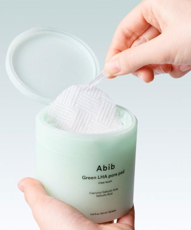 ABIB  Green LHA Pore Pad Clear Touch 60 Sheets, main tenant des pads verts à côté du pot, contexte soin visage.