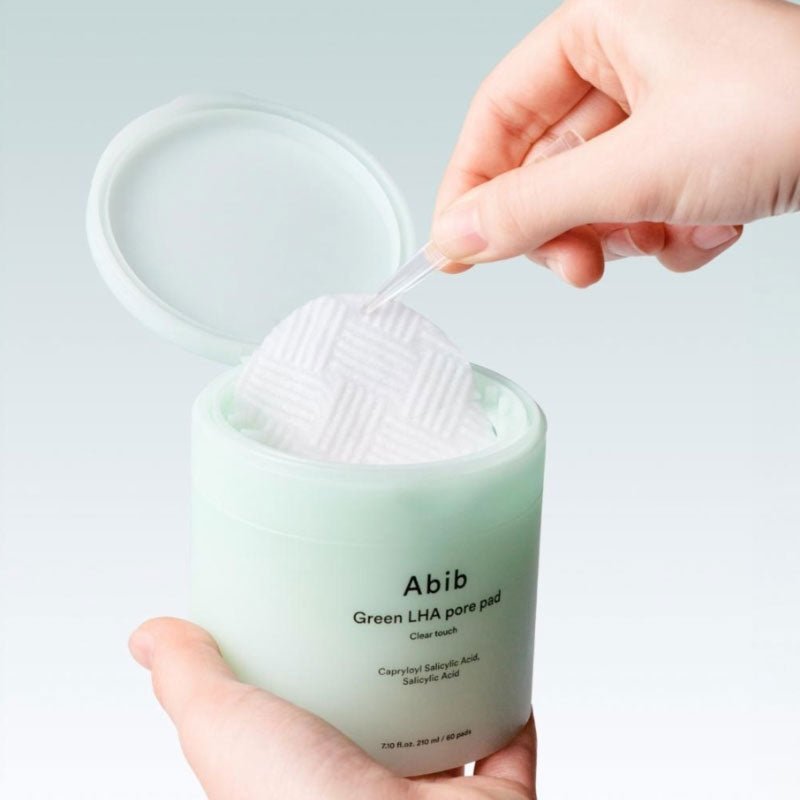 ABIB  Green LHA Pore Pad Clear Touch 60 Sheets, main tenant des pads verts à côté du pot, contexte soin visage.
