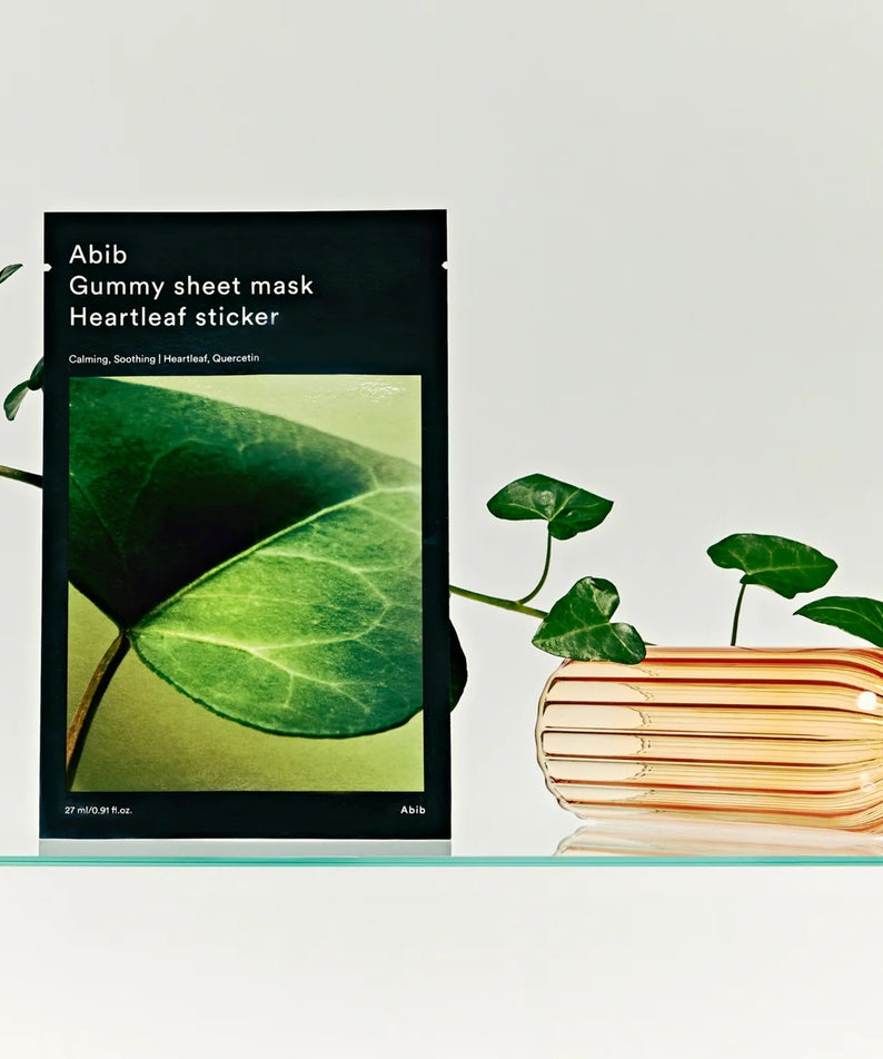 ABIB Gummy Sheet Mask Heartleaf Sticker Abib, photo produit avec feuilles vertes et pile de livrets sur fond clair.