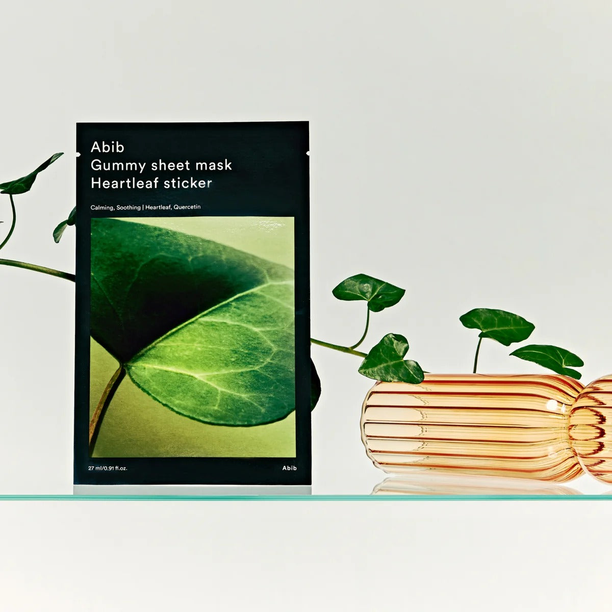 ABIB Gummy Sheet Mask Heartleaf Sticker Abib, photo produit avec feuilles vertes et pile de livrets sur fond clair.