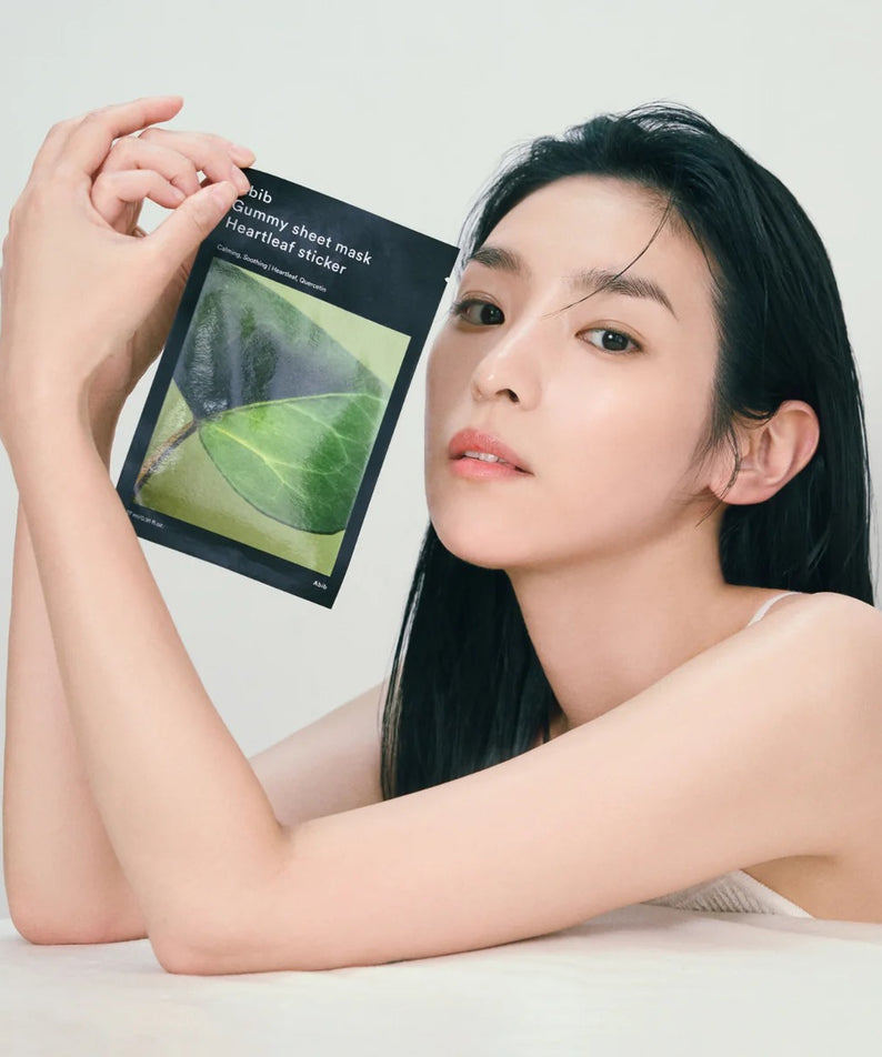 Femme appliquant ABIB Gummy Sheet Mask Heartleaf Sticker : masque feuille cœurleaf, produit ABIB sur fond clair.