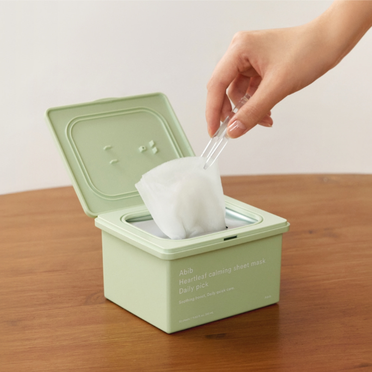 ABIB  Heartleaf Calming Sheets Mask Daily Pack 30 Sheets : main pose un masque en tissu apaisant sur table, boîte verte