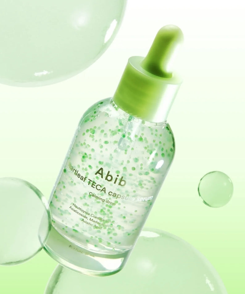 Décris l'image en français : ABIB Heartleaf TECA Capsule Serum Calming Drop 50ml sur fond vert avec gouttes et flacon.
