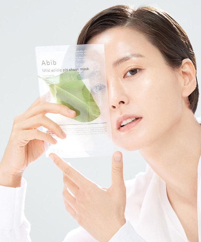 ABIB Mild Acidic pH Sheet Mask 30ml : femme appliquant un masque feuille sur le visage, emballage ABIB en arrière-plan