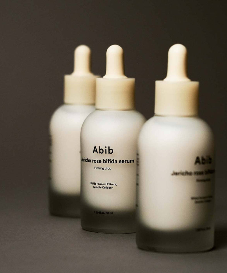 Trois flacons du ABIB Resurrection Bifida Serum Firming Drops 50ml sur fond gris, mettant en valeur son design élégant et minimaliste.