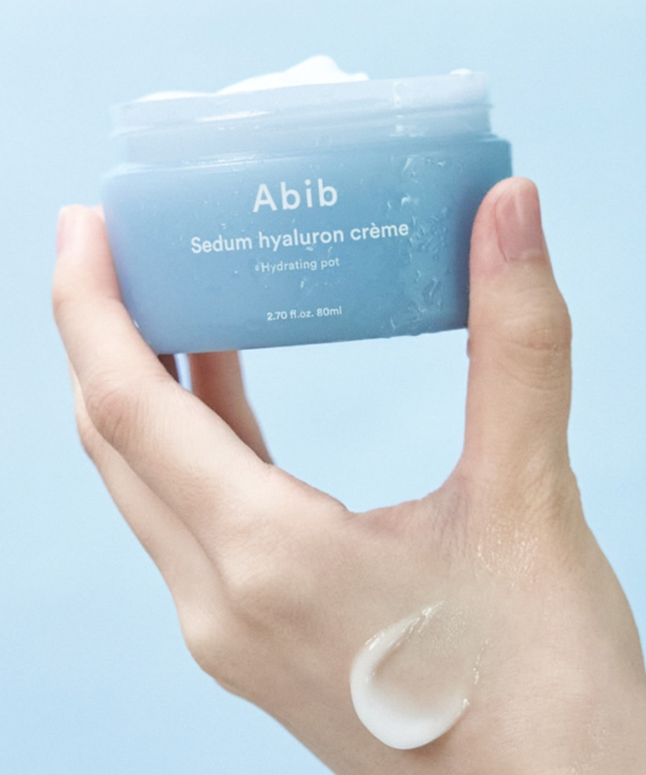 Crème hydratante ABIB Sedum Hyaluron Creme Hyadrating Pot 80ml tenue dans la main, fond bleu apaisant.