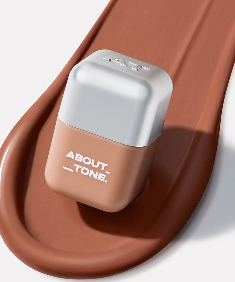 ABOUT TONE Blur Fit Tint Mini 2.3g, tube beige sur base brune, photo produit maquillage en gros plan.