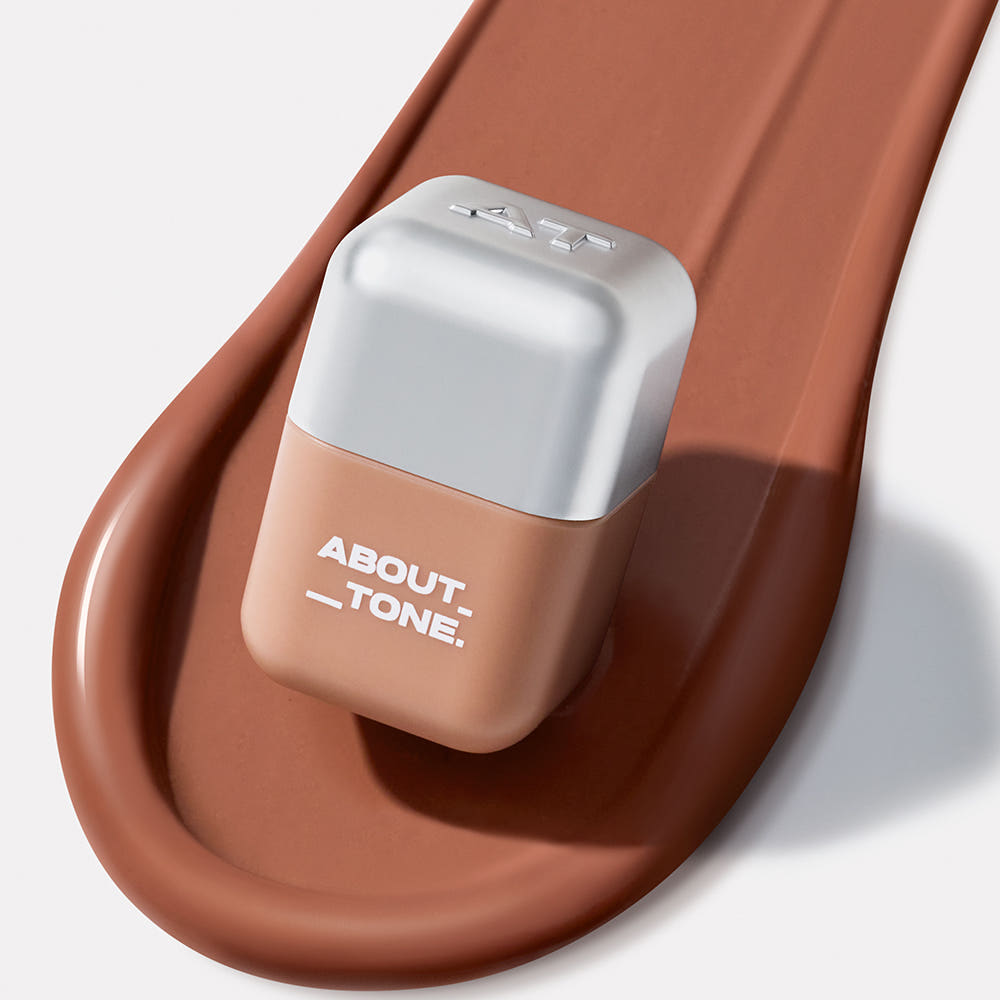 ABOUT TONE Blur Fit Tint Mini 2.3g, tube beige sur base brune, photo produit maquillage en gros plan.