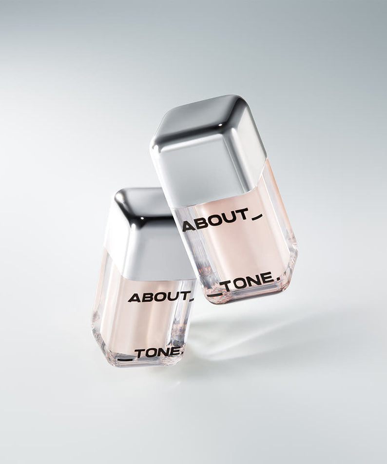 Deux flacons de ABOUT TONE Skin Layer Cover Fit Concealer 5.6g avec bouchons en argent sur fond gris élégant.