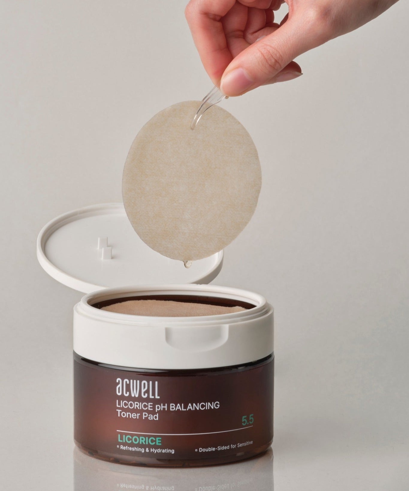 ACWELL Licorice pH Balancing Toner Pad 70P : pad beige en main au-dessus du pot, fond clair, marque ACWELL, beauté