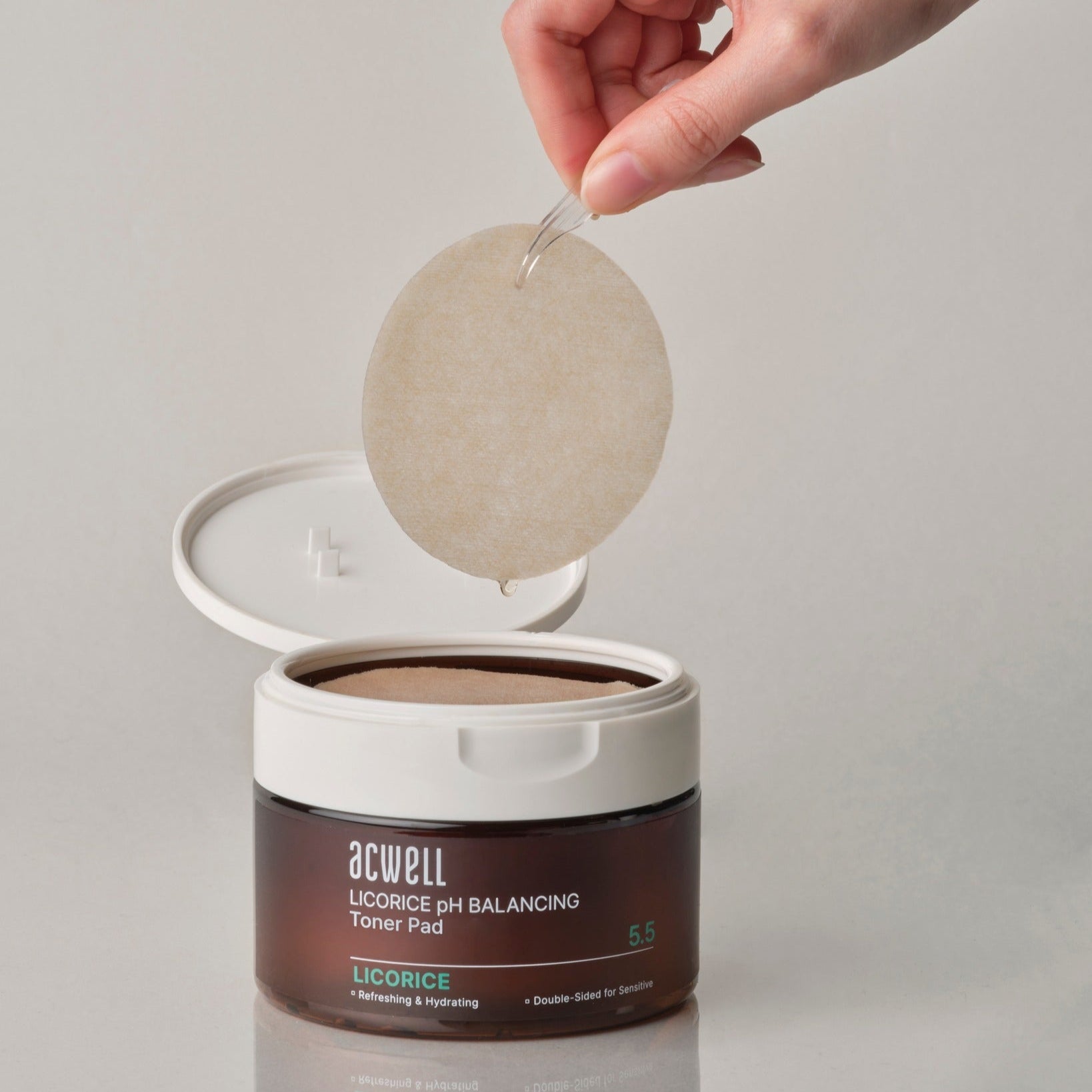 ACWELL Licorice pH Balancing Toner Pad 70P : pad beige en main au-dessus du pot, fond clair, marque ACWELL, beauté