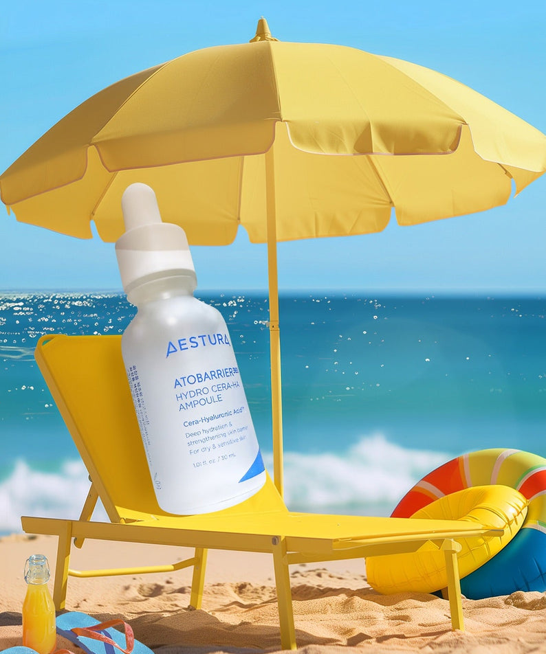 AESTURA Atobarrier 365 Hydro Cera-HA Ampoule 30ml sur une chaise longue de plage sous un parasol jaune, mer en arrière-plan.