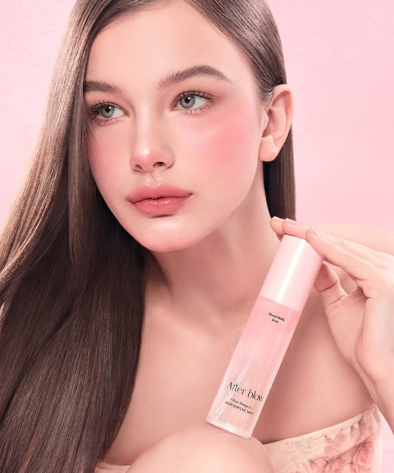 Femme tenant un flacon de AFTER BLOW Hair Perfume Mist 80ml devant un fond rose, parfait pour parfumer les cheveux et ajouter de l'élégance.