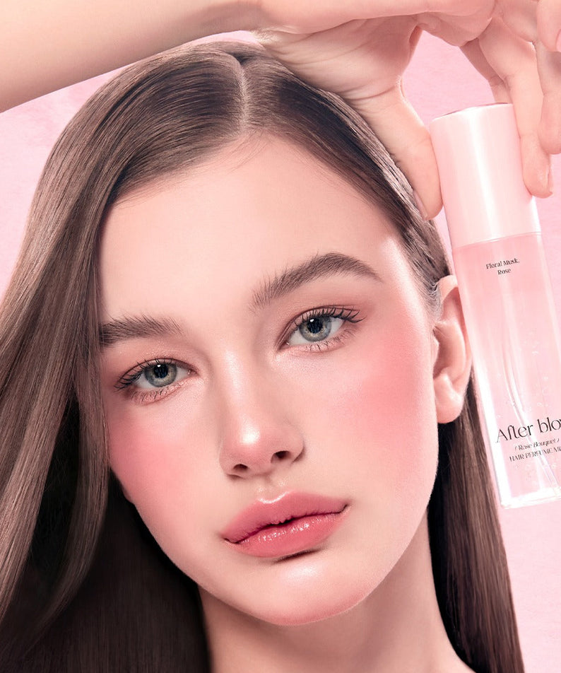 Femme tenant un flacon de AFTER BLOW Hair Perfume Mist 80ml sur fond rose, soin capillaire parfumé.