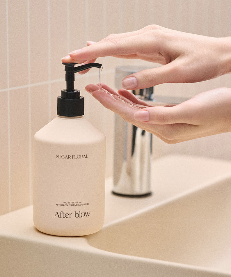 AFTER BLOW Perfume Hand Wash Sugar Floral 400ml sur un lavabo, les mains en train de l'utiliser, ambiance florale et rafraîchissante.