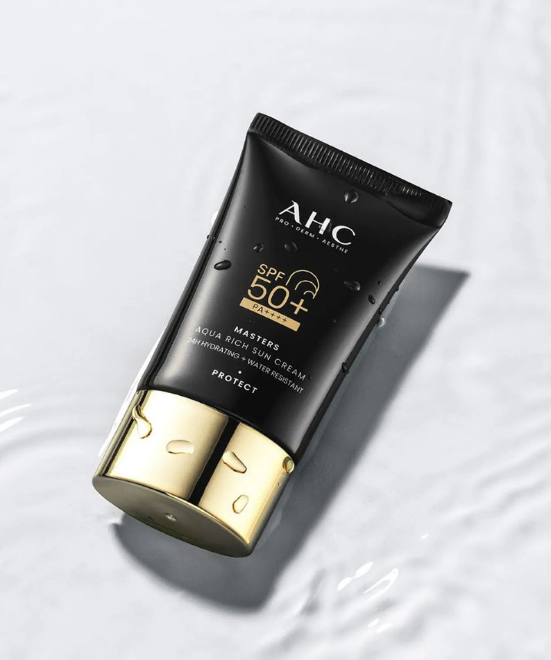 AHC Masters Aqua Rich Sunscreen 50ml de AHC, tube noir SPF 50+ sur fond clair avec gouttelettes d’eau, visuel produit.