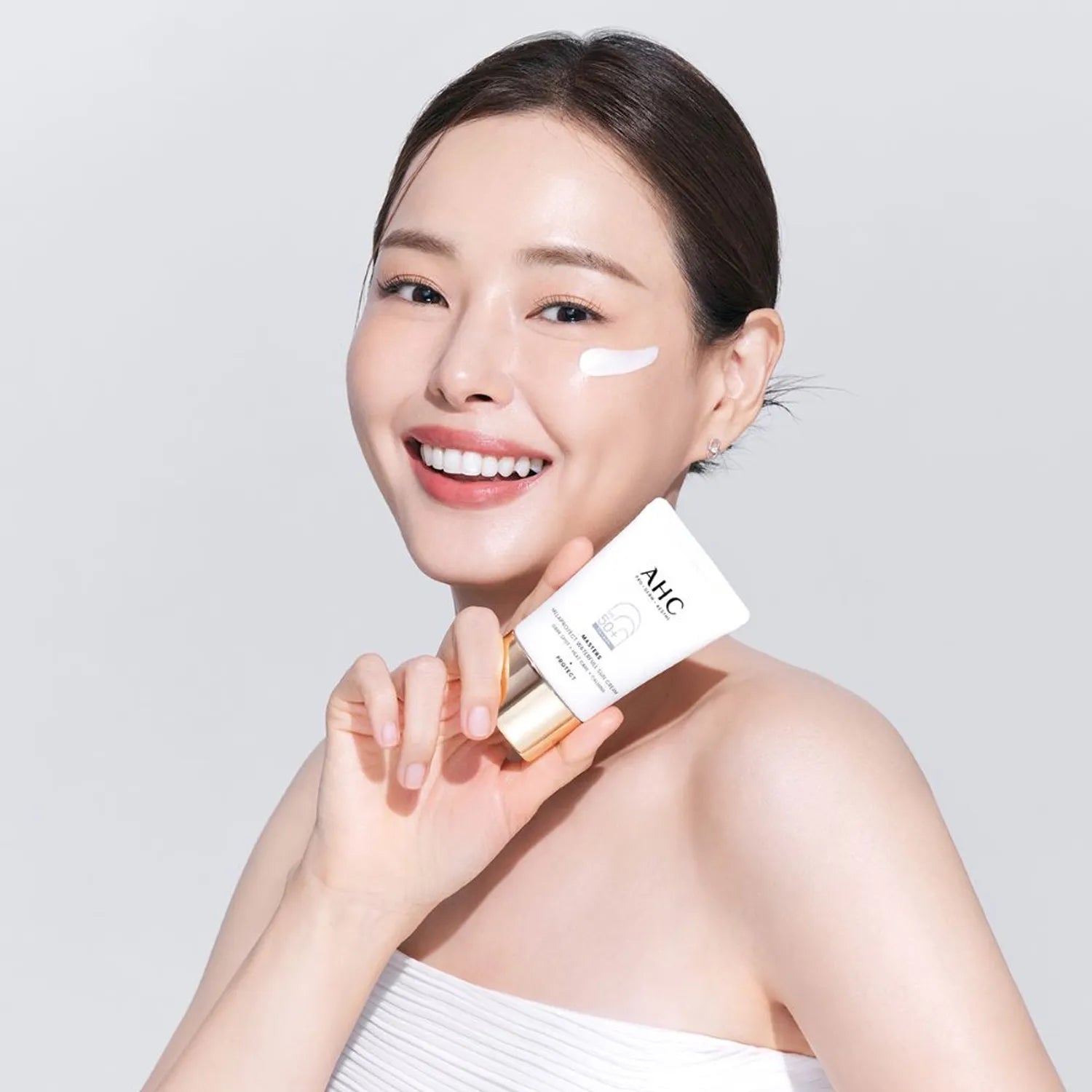 AHC Masters Mela Protect Waterfull Sunscreen 40ml, crème solaire AHC sur peau, femme souriante studio blanc.