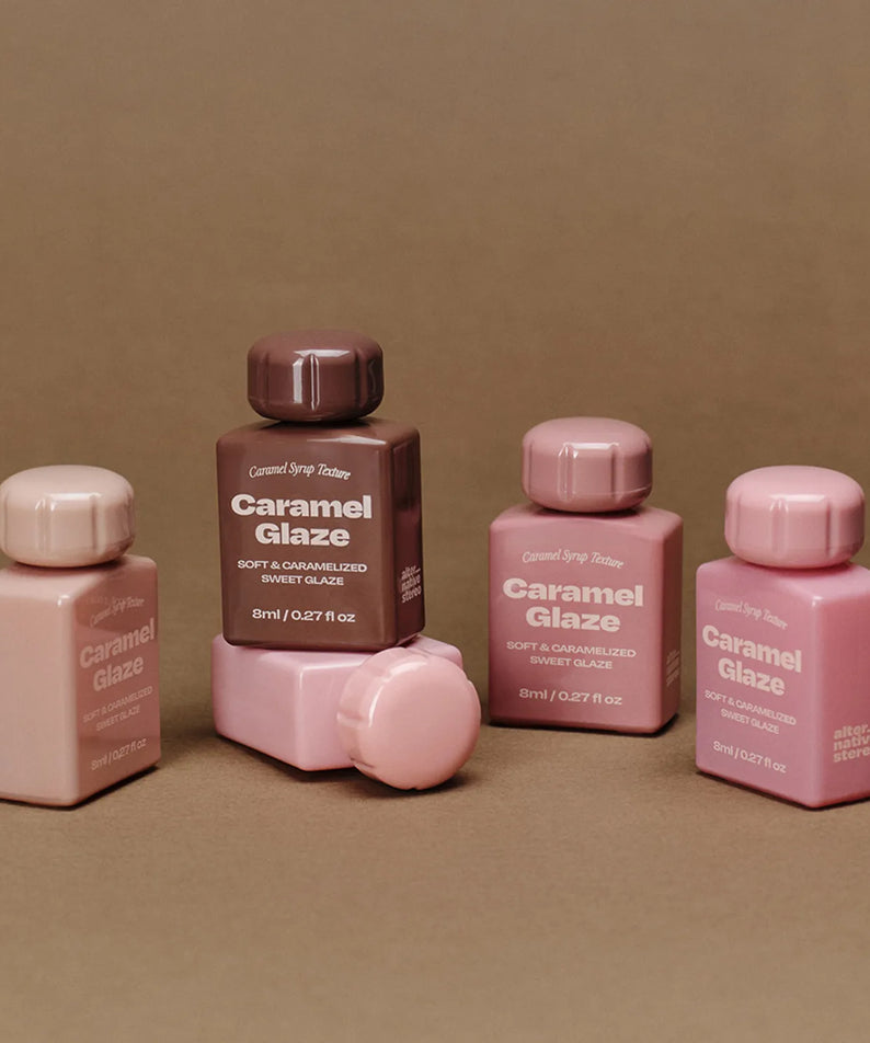 Décris l'image en français : ALTERNATIVE STEREO Lip Potion Caramel Glaze (7 colors), flacons caramel, fond beige.