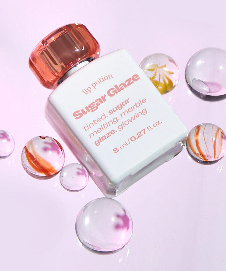 Produit cosmétique ALTERNATIVE STEREO Lip Potion Sugar Glaze avec flacon blanc et bouchon rose, décoré de perles brillantes.