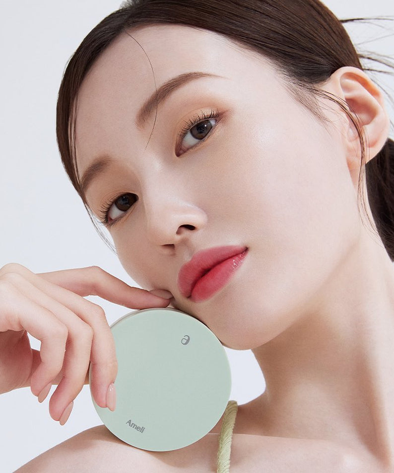 Femme tenant AMELI Complement Series Cushion SPF42 PA++ Green, maquillage lumineux et naturel.