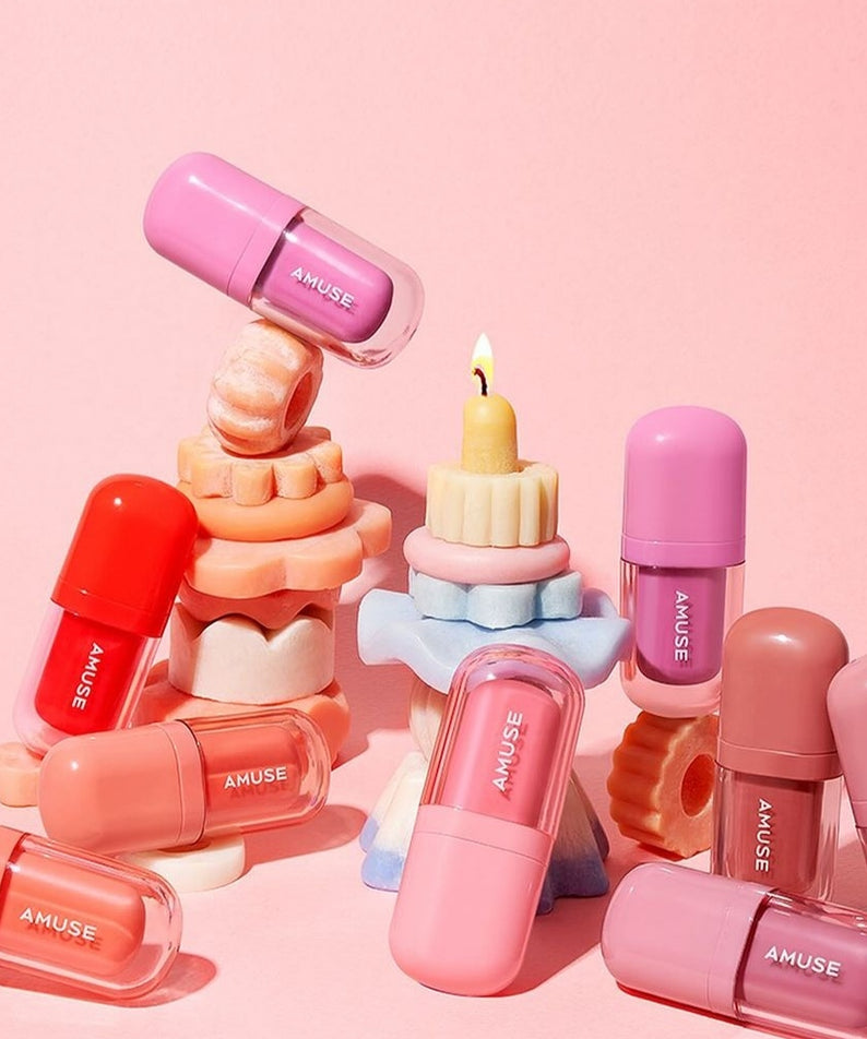 Rouges à lèvres AMUSE BEBE TINT sur fond rose, présentation colorée et élégante.