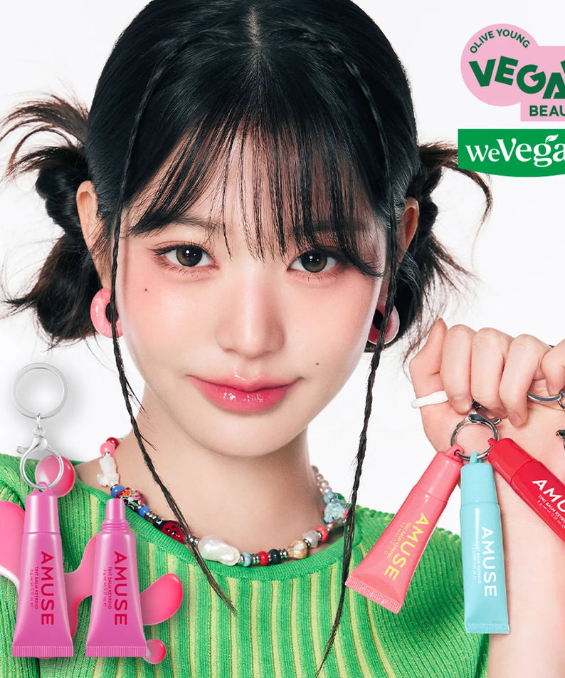 Femme souriante tenant des porte-clés AMUSE TINT BALM KEYRING avec produits amusants et design vegan. Beauté éthique et colorée.