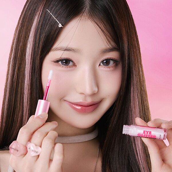 AMUSE Eye Glitter Volume Fixer AMUSE sur photo beauté: femme aux yeux brillants tenant le produit, fond rose.