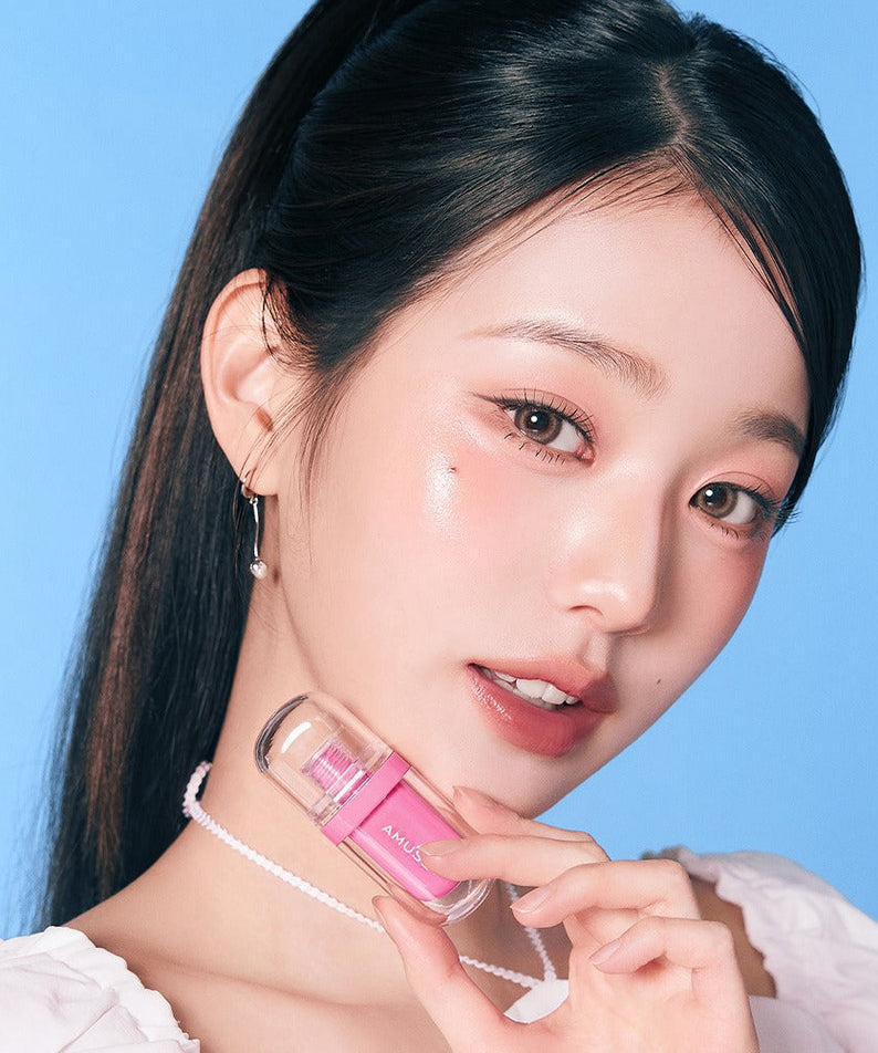 AMUSE Jel-Fit Tint : femme tenant le produit maquillage en gel, gros plan sur peau éclatante fond bleu ciel.