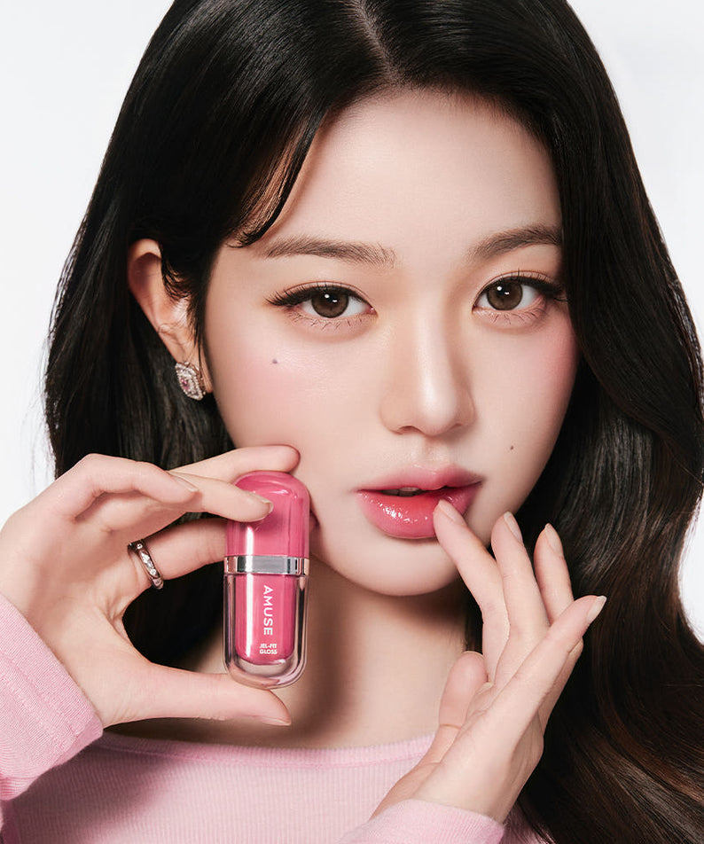 Femme tenant AMUSE Jel Fit Gloss rose, maquillage élégant et moderne.