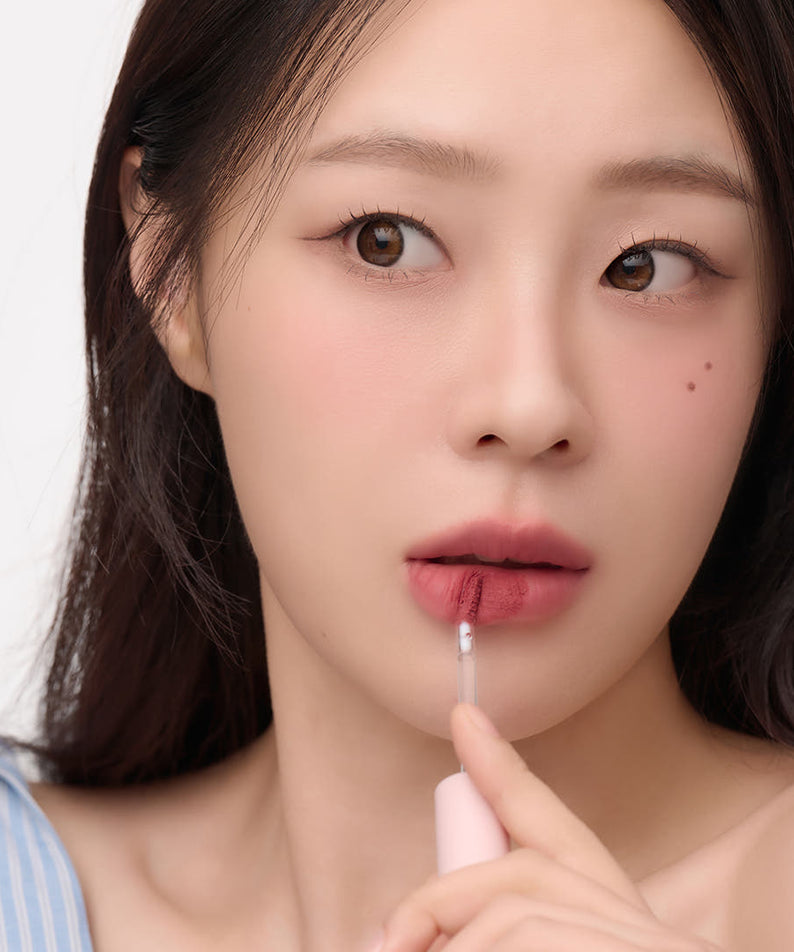 Femme appliquant AND:AR Matte Lip Color, rehausse ses lèvres d'une couleur mate élégante et sophistiquée.