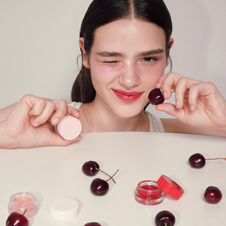 ANILLO Mellow Glow Balm : jeune femme applique un baume rosé, pack cosmétique sur table avec ingrédients, visuel beauté.
