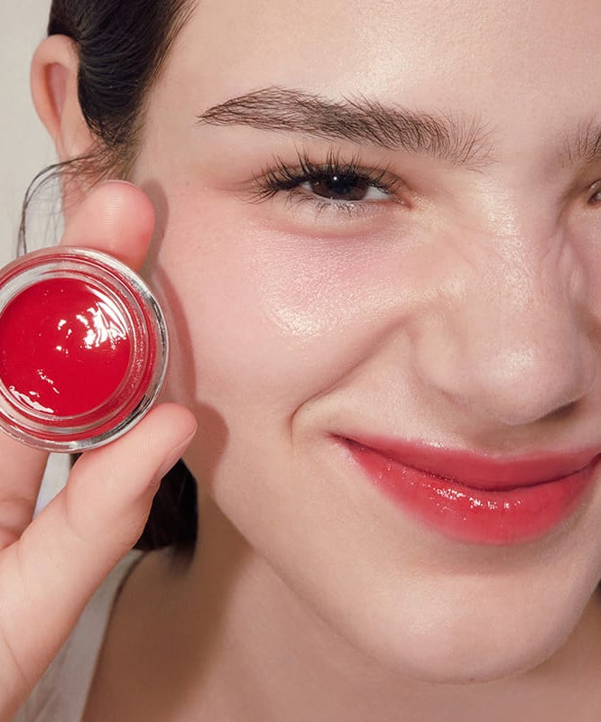 ANILLO Petal Glow Balm, baume à lèvres rouge en pot, gros plan sur visage maquillé, main tenant le produit, contexte beauté.