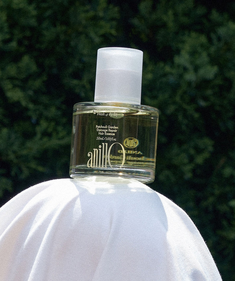 ANILLO Patchouli Garden Damage Repair Hair Essence 50ml, flacon vert sur fond jardin, marque ANILLO, cheveux réparation