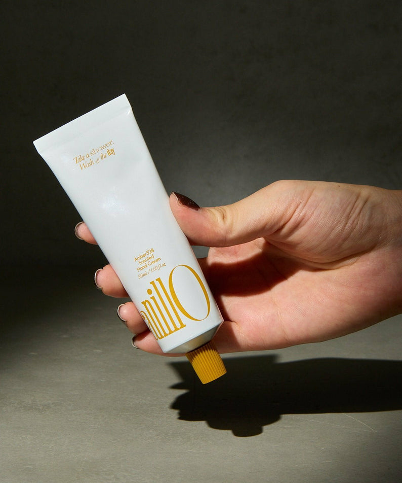 ANILLO Amber528 Scented Hand Cream 50ml en main, tube blanc et ambiance sobre sur fond gris foncé, marque ANILLO