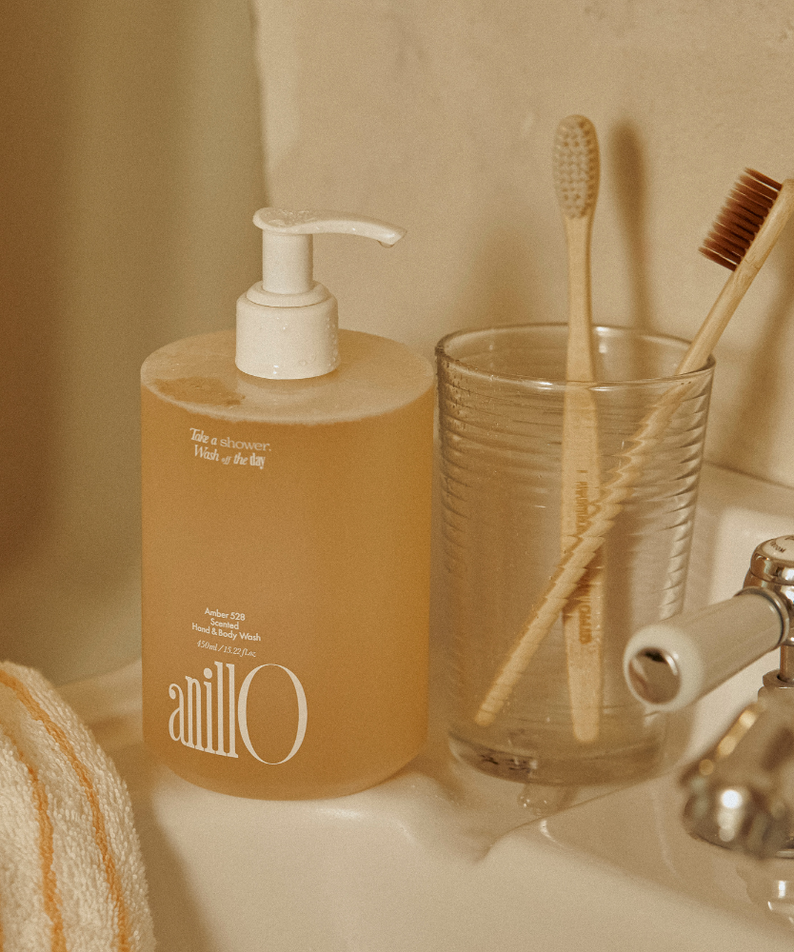 Décris l'image en français : ANILLO Amber528 Scented Hand & Body Wash 450ml, marque sur flacon, salle de bain beige.