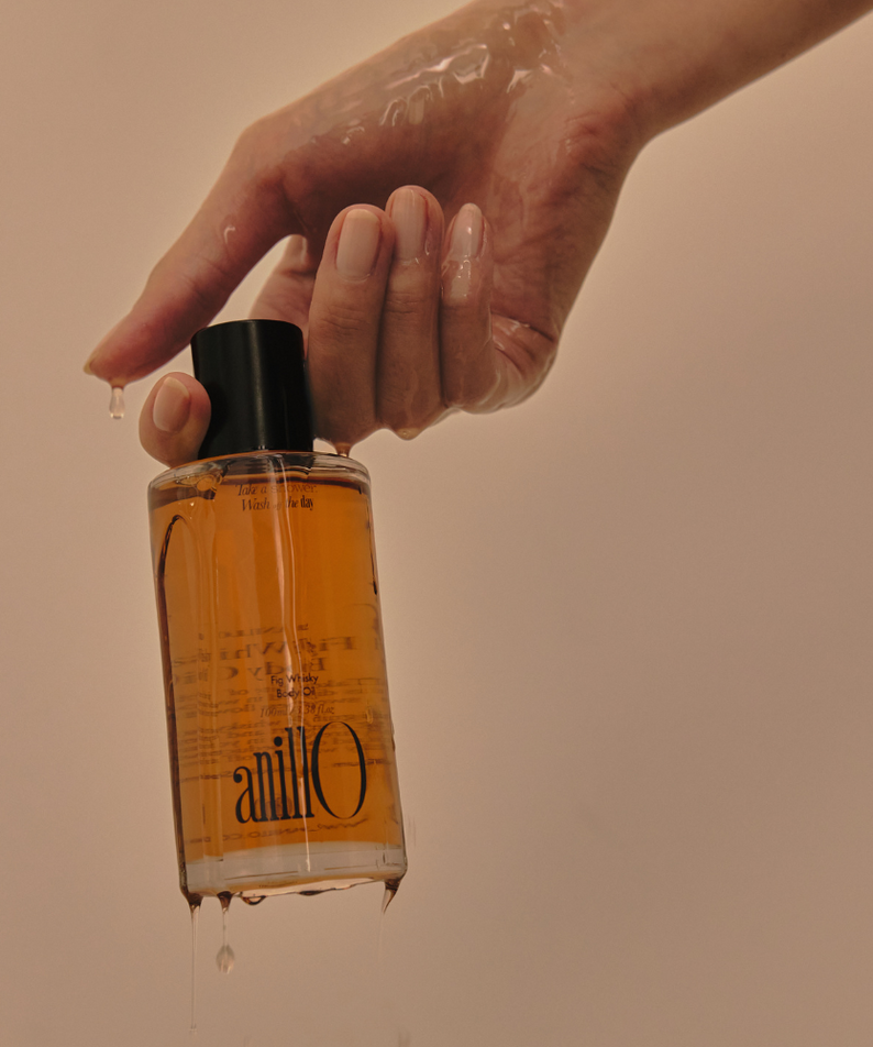 ANILLO Fig Whisky Body Oil 100ml, flacon tenu par une main, ambiance chaude, contexte soin beauté à la figue.