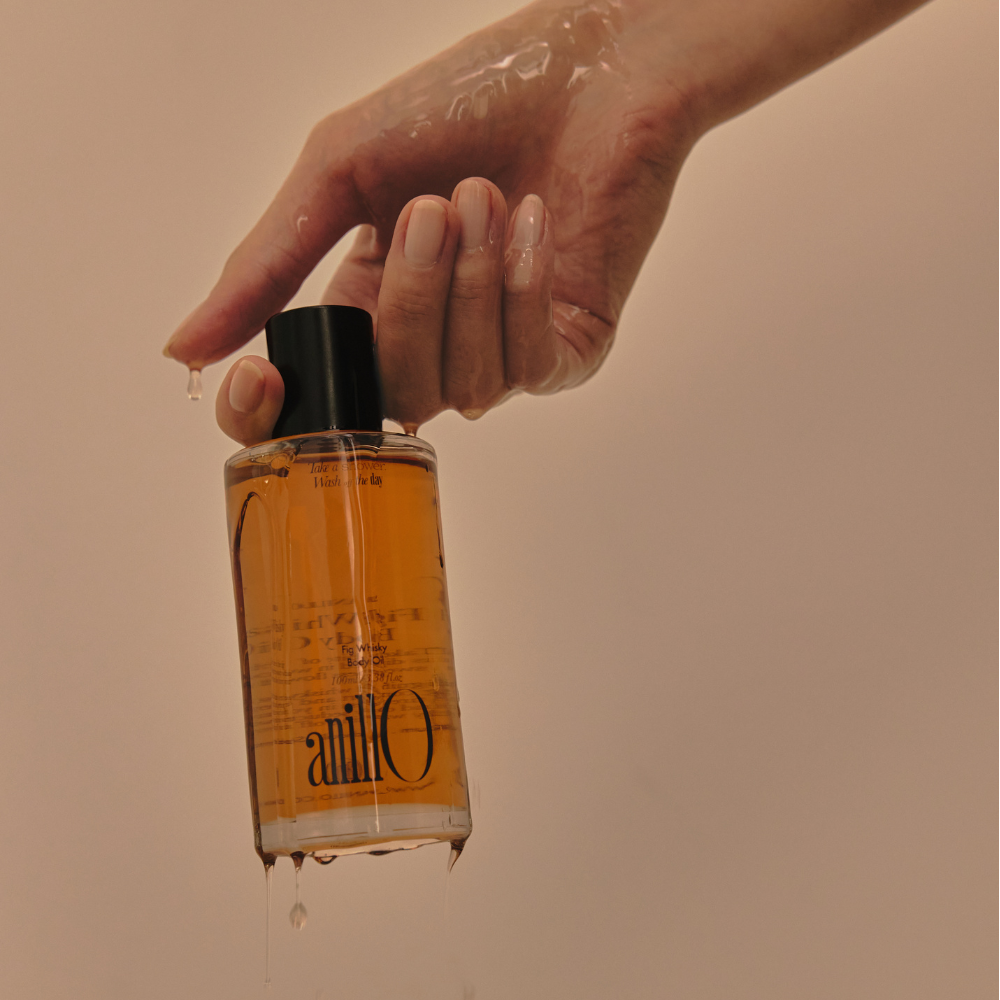 ANILLO Fig Whisky Body Oil 100ml, flacon tenu par une main, ambiance chaude, contexte soin beauté à la figue.