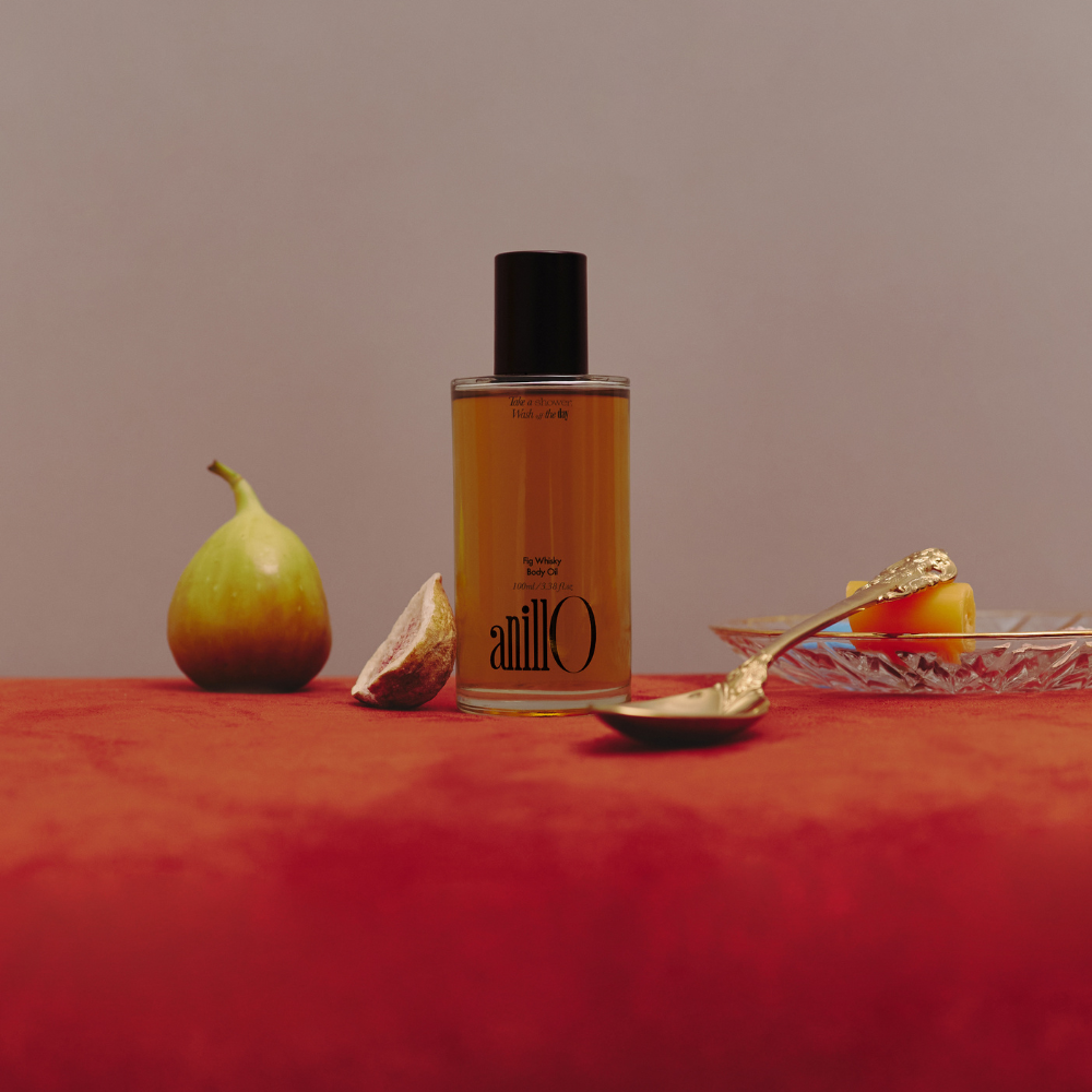 ANILLO Fig Whisky Body Oil 100ml, bouteille sur fond beige avec figues et ambiance spa, marque ANILLO, scène visuelle