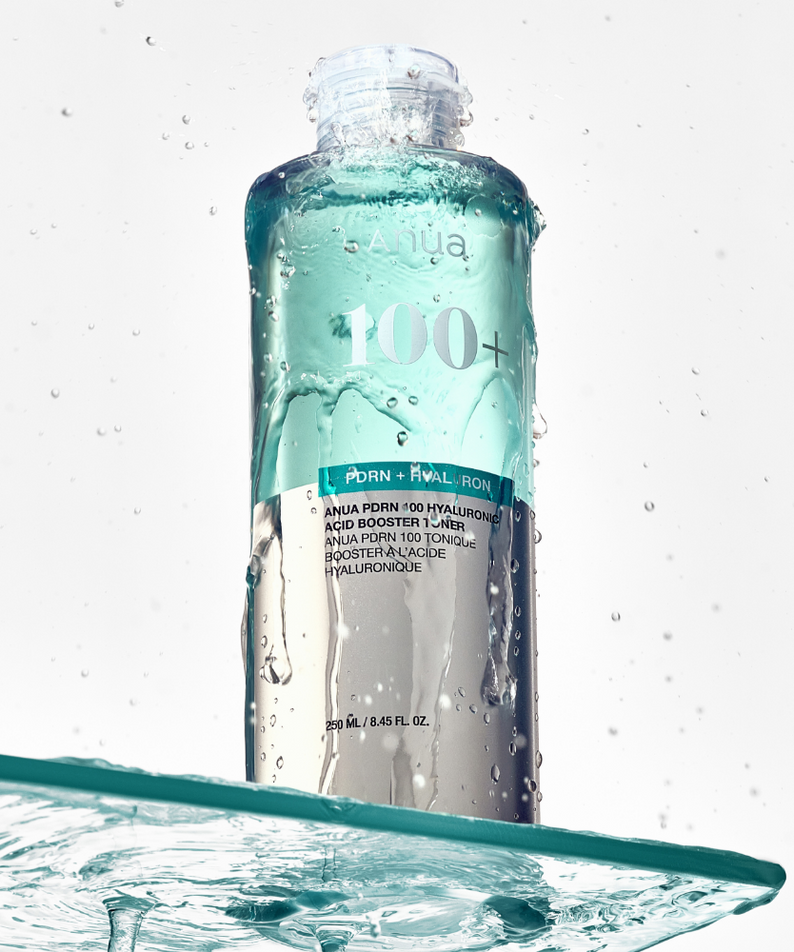 ANUA PDRN 100 Hyaluronic Acid Booster Toner 250ml, bouteille sur fond blanc avec éclaboussures d’eau, style skincare.