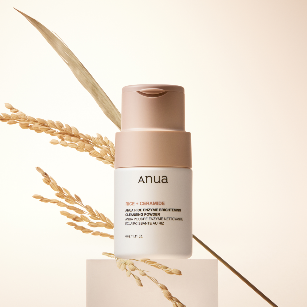 ANUA Rice + Ceramide Brightening Cleansing Powder 40g, marque ANUA, flacon crème sur podium avec grains de riz en arrière-plan.